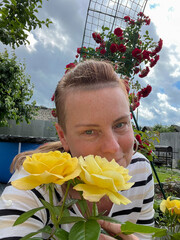 50 year old woman poses in her garden with roses in the background.