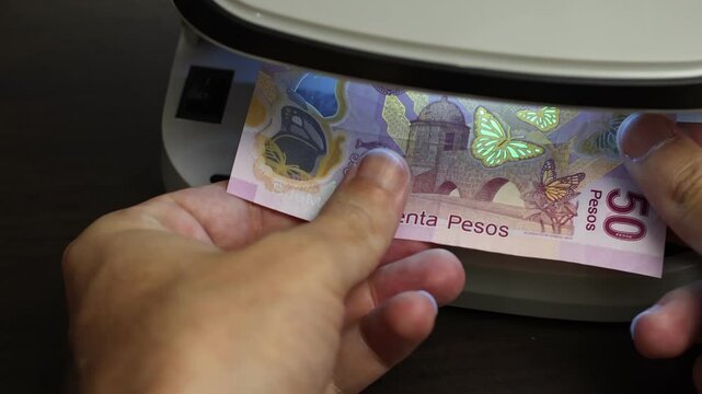 Examination of Mexican Peso (MXN) cash money with UV counterfeit detector. Concept of authenticity check, fight against counterfeiting of banknotes, anti fraud measures in Mexico. Close up view.
