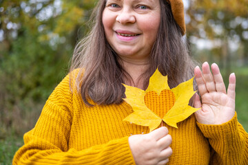 Happy mature woman with fall leaf in hand, Elegant senior lady, park background, vibrant aging,...