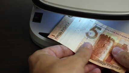 Examination of belarussian ruble (BYN) cash money with UV counterfeit detector. Concept of authenticity check, fight against counterfeiting of banknotes, anti fraud measures in Belarus. Close up view.
