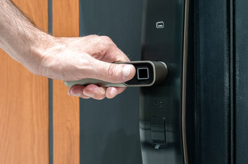 Close-up of male hand about to press fingerprint scanner on smart door lock, concept of secure...