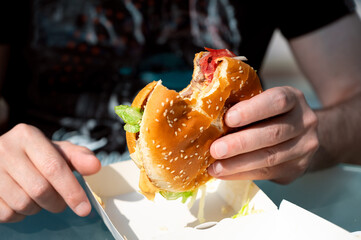 Close-up of a juicy beef burger in a man's hand, appetizing fast food scene evoking hunger and...