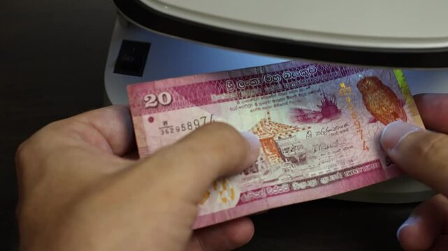 Examination of Sri Lanka rupee (LKR) cash money with UV counterfeit detector. Concept of authenticity check, fight against counterfeiting of banknotes, anti fraud measures in Sri Lanka. Close up view.