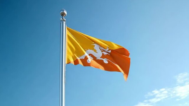 A vibrant flag of Bhutan flutters on a tall flagpole under a bright blue sky, showcasing its distinct colors and intricate design.