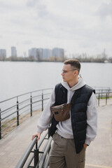 a handsome man of European appearance stands on the embankment in a big city against the background of a river
