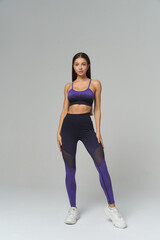 Young woman stands confidently in a matching sports outfit, consisting of a purple sports bra and...