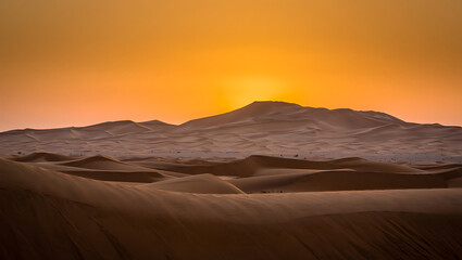 Naklejka premium Golden desert dunes at sunset with mountain silhouette sand