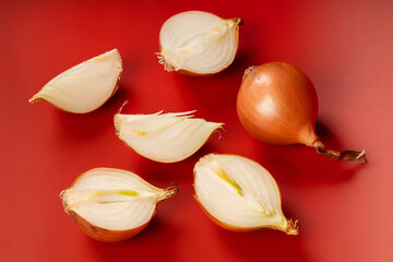 Composition of whole and halved onions placed on a vibrant red surface.