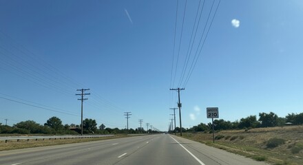 Fototapeta premium Sunny highway scene with power lines, clear blue sky, and speed limit sign