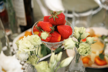 Vibrant strawberries fill a glass bowl surrounded by elegant white flowers, creating an appealing...