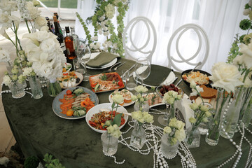 Elegant banquet table set with a variety of gourmet dishes and floral decor. Plates feature appetizing meals, surrounded by wine bottles and delicate flower arrangements, creating a luxurious dining e