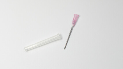 Sterile hypodermic needle with pink hub placed next to its transparent protective cap on a white...