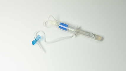 Butterfly blood collection needle connected to a holder containing a blue top vacuum tube. Medical equipment used for venipuncture and laboratory diagnostics, on white background.