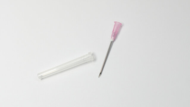 Sterile hypodermic needle with pink hub placed next to its transparent protective cap on a white background. The needle is exposed, clean, and ready for medical use.