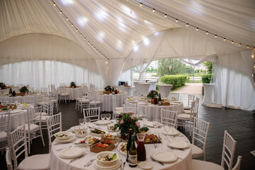 Elegant indoor event setting featuring round tables with white linens and arranged floral...