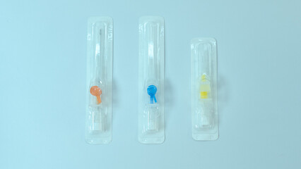 Three color-coded intravenous cannulas sealed in sterile plastic packaging, aligned vertically on a...