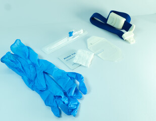 IV medical kit with gloves, alcohol pad, gauze, cannula, dressing, and tourniquet arranged on white...