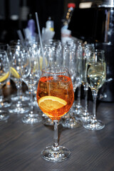 Vibrant orange cocktail garnished with a fresh orange slice on a bar table, surrounded by an array of empty wine glasses, ready for an event or celebration with drinks.