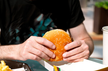 Man about to bite into juicy unhealthy burger, real street food moment with craving and guilty...