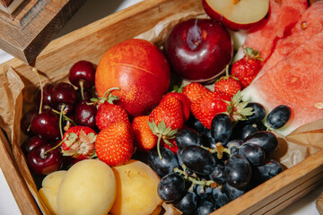 Fresh assortment of colorful fruits including strawberries, grapes, cherries, watermelon, and more in a wooden box, highlighting freshness and vibrant natural textures.