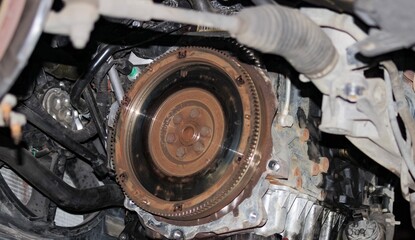 Close-up of car flywheel inside engine bay with visible rust and heat marks, mechanical components,...