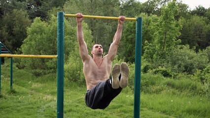 Athletic man trains abdominal muscles raising legs on horizontal bar at sports ground. Young...