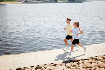 Couple enjoys morning run along serene riverside pathway under bright blue sky in vibrant urban...