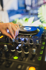 Close-up of DJ hand adjusting knobs on mixer with vibrant LED lights, turntable and sound...