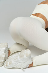 White activewear-clad person kneeling with focus on textured leggings and sneakers. The shot highlights fitness attire. No text present