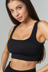 Young woman with long brown hair in a ribbed black crop top, posing confidently. She has fair skin...