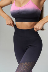 Woman adjusting high-waisted athletic leggings wearing a pink and black sports bra, fishnet accents...