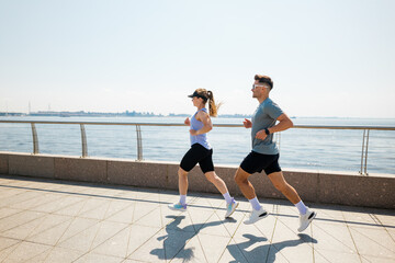 Couple enjoys an energizing run along the waterfront on a sunny day, embracing fitness and nature...