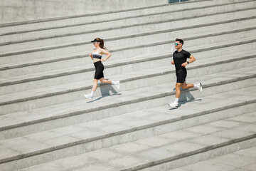 Couple running up outdoor stairs under bright sunlight, showcasing fitness and determination during a morning workout session