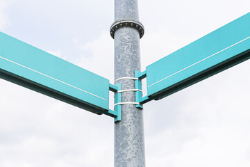 Empty turquoise street signs on a metal pole. Urban road signage with copy space. Blank directional boards on galvanized post. Clear sky background. Navigation element for city information.
