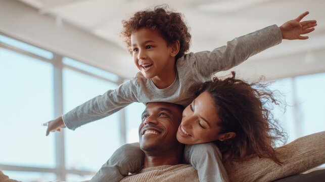 Cheerful indian son sitting on father shoulder playing at home with african mother. Playful little boy enjoying spending time with parents at home. Flying child enjoying playing with his ethnic famil