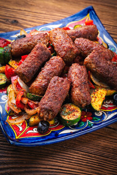 Traditional Croatian cevapi spicy meat ball rolls with troasted vegetables served as close-up on rustic design plate