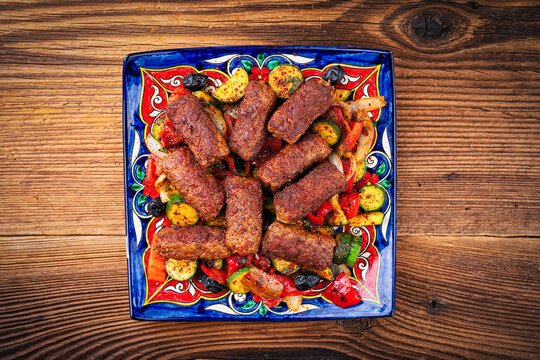 Traditional Croatian cevapi spicy meat ball rolls with troasted vegetables served as top view on a rustic design plate