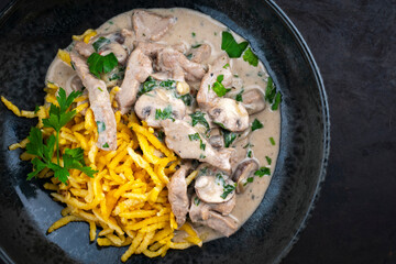 Traditional Swiss Zürcher geschnetzeltes from veal with mushrooms spaetzle in cream sauce served as top view in a design bowl