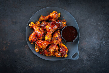 Authentical barbecue chicken drumsticks with hot chili sauce as marinade served as top view on a design plate with copy space