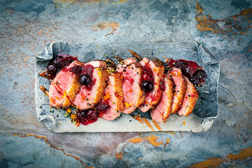 Traditional duck breast roast slices with orange and cranberry sauce served as top view on a stone...