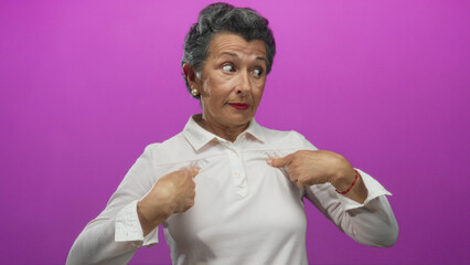 Woman pointing at herself against a vivid pink background with a surprised expression and grey...