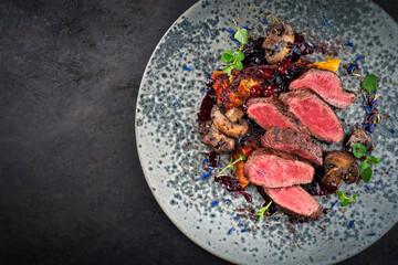 Barbecue dry aged venison steaks - deer entrecote cut English roasted with grilled mushrooms, fruit berry gravy sauce and panettone herbs served as top view on a design plate with copy space left