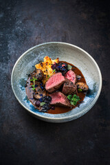 Barbecue dry aged venison steaks - deer entrecote cut english roasted served with grilled mushrooms, fruit berry gravy sauce and panettone herbs served as close-up on a design plate