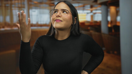 Woman places hand on forehead in a facepalm inside a restaurant where glasses frame a young latin...