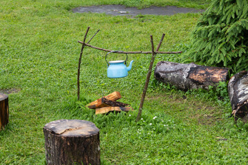 Outdoor camping setup with blue kettle hanging over a campfire