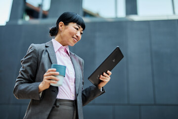 Portrait of a young asian japanese businesswoman woman using a tablet computer and holding a cup of...