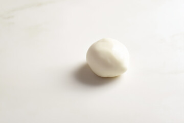 Mozzarella ball placed in the middle of white surface, slight sheen, soft natural lighting