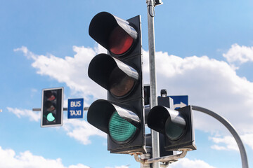Urban traffic lights against blue sky with white clouds. Green signal glowing on city street....