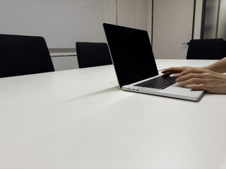 Hands typing on laptop in empty modern meeting room