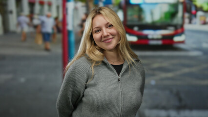 Woman smiling in city street with blurred pedestrians and bus in the background suggests a lively...
